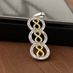 May include: A silver pendant with three stacked circles, each containing a gold number eight. The circles are encrusted with small, clear stones. The pendant has a silver bail at the top for a chain.