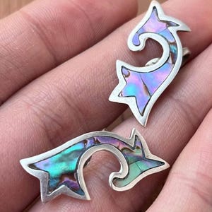 May include: A pair of sterling silver earrings with an abalone shell inlay. The earrings have a stylized, curved design with star-shaped elements and iridescent colors of blue, green, and purple.