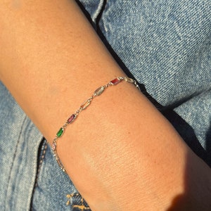 May include: A silver chain bracelet with colorful rectangular stones. The stones are in shades of green, blue, pink, and red.