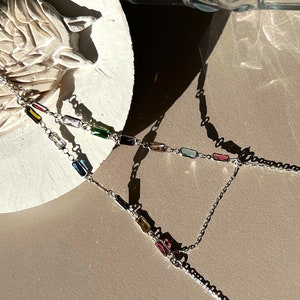 May include: Two silver chains with colorful rectangular gemstones. The chains are layered and have a delicate, feminine look.