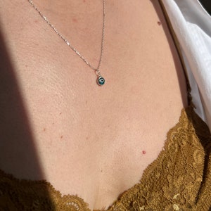 Puede incluir: Un collar de cadena de plata con un peque&ntilde;o dije de ojo turco azul.
