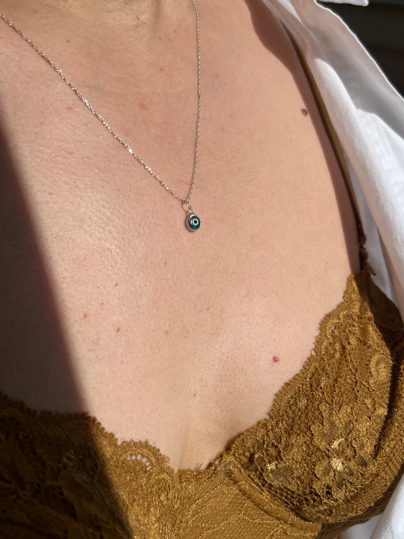 Puede incluir: Un collar de cadena de plata con un peque&ntilde;o dije de ojo turco azul.