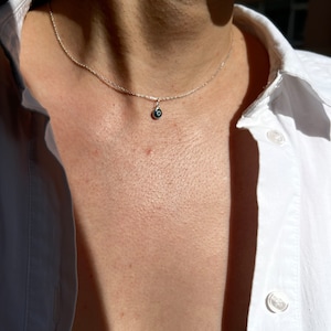 Puede incluir: Un collar de cadena de plata con un peque&ntilde;o dije de ojo turco azul.