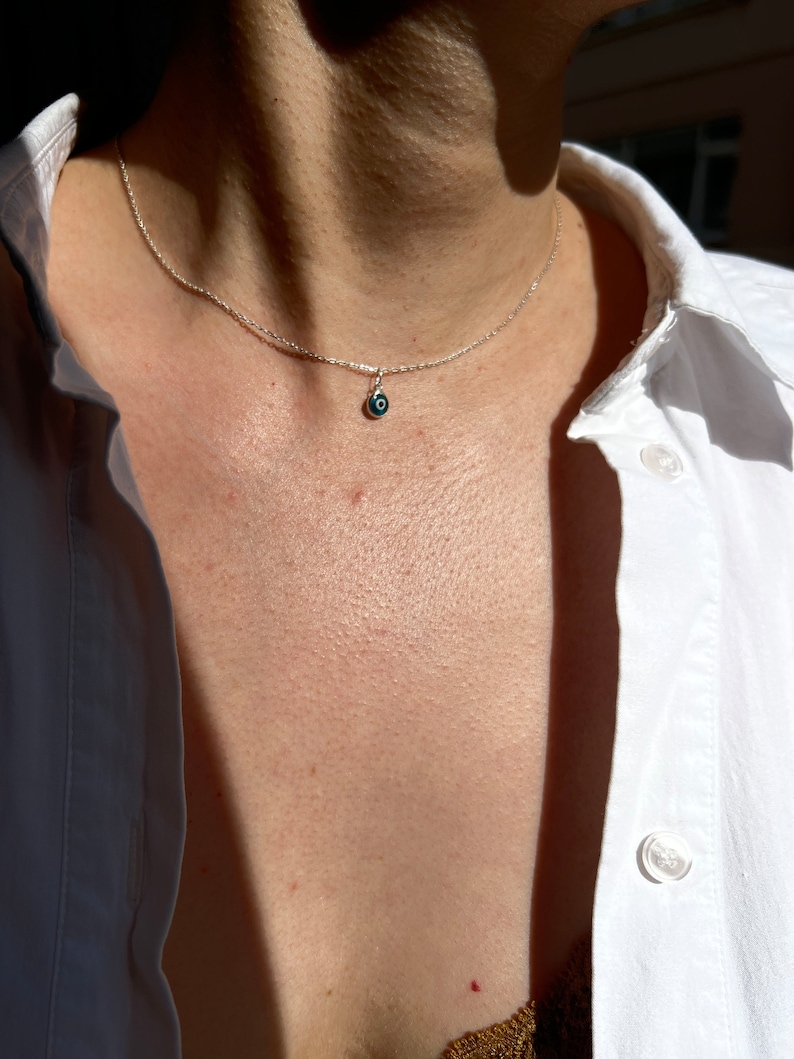 Puede incluir: Un collar de cadena de plata con un peque&ntilde;o dije de ojo turco azul.