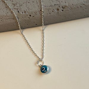 Puede incluir: Un collar de cadena de plata con un peque&ntilde;o dije de ojo turco azul.