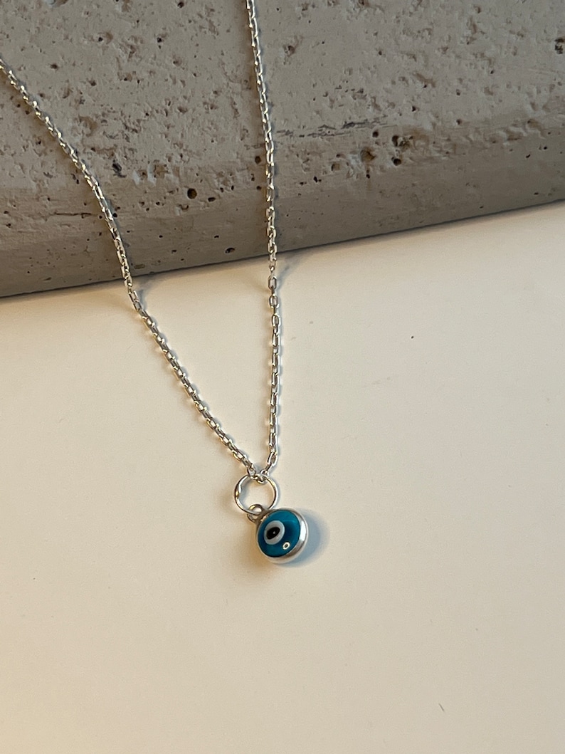 Puede incluir: Un collar de cadena de plata con un peque&ntilde;o dije de ojo turco azul.