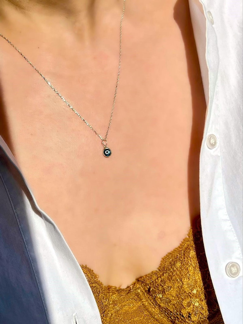 Puede incluir: Un collar de cadena de plata con un peque&ntilde;o dije de ojo turco azul.