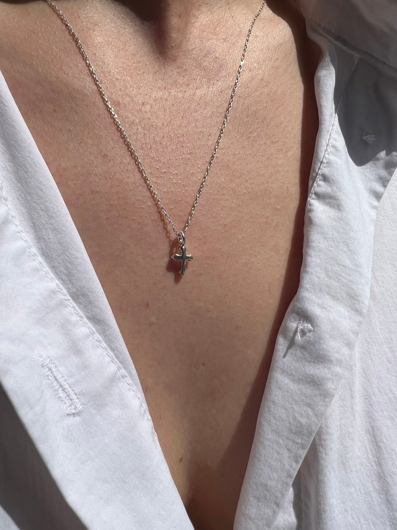 May include: A silver chain necklace with a small silver cross pendant.