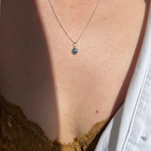 Puede incluir: Un collar de cadena de plata con un peque&ntilde;o colgante azul de ojo turco.