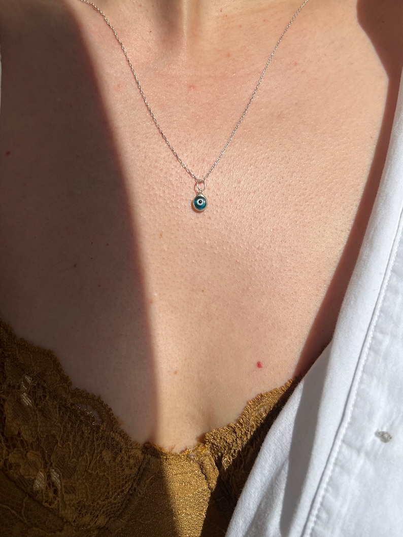 Puede incluir: Un collar de cadena de plata con un peque&ntilde;o colgante azul de ojo turco.