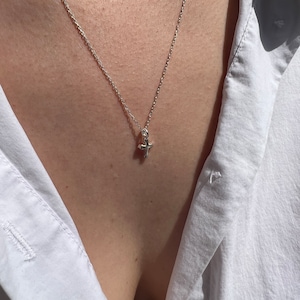 May include: A silver chain necklace with a small, silver cross pendant.