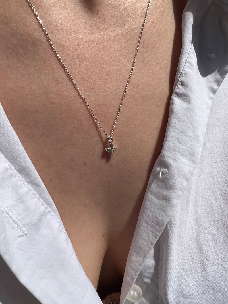 May include: A silver chain necklace with a small, silver cross pendant.