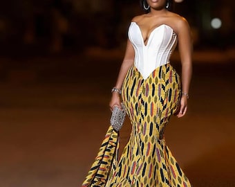 May include: A woman wearing a white strapless corset top and a yellow, black and red patterned skirt with a long train. The skirt has a mermaid silhouette.