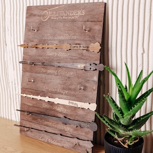 May include: A brown wooden wall display board featuring the Ollivander's logo and engraved names of characters including Albus Dumbledore, Harry Potter, Hermione Granger, Severus Snape, Draco Malfoy, Bellatrix Lestrange, and Lord Voldemort.