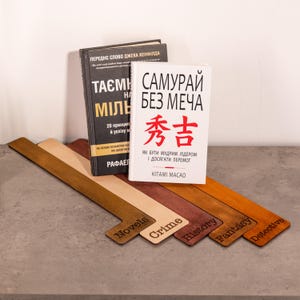 May include: Books and wooden bookmarks are displayed. The books have text in Ukrainian and Japanese. The bookmarks are labeled "Novels", "Crime", "History", "Fantasy", and "Detective". The bookmarks are various shades of brown.