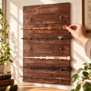 May include: A dark brown wooden wall display board featuring the Ollivander's logo and six horizontal rows. Each row displays a wooden wand replica and a name: Albus Dumbledore, Harry Potter, Hermione Granger, Severus Snape, Draco Malfoy, Bellatrix Lestrange, and Lord Voldemort.