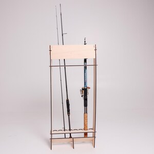 May include: A wooden fishing rod rack with three fishing rods. The rack is made of light-colored wood and has a rectangular frame. The fishing rods are black and blue, with cork handles and silver reels. The rack is designed to hold multiple fishing rods.