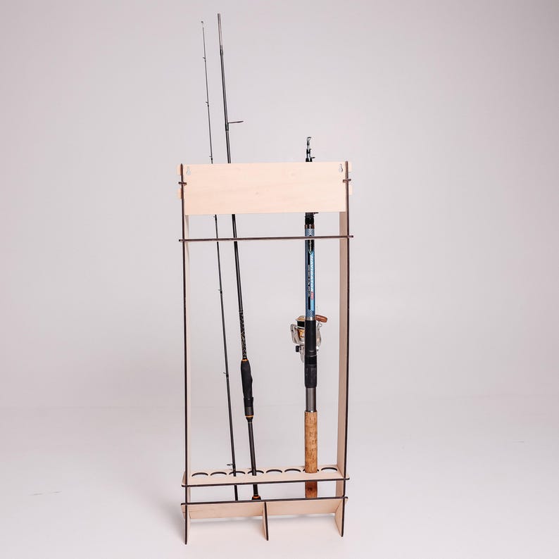 May include: A wooden fishing rod rack with three fishing rods. The rack is made of light-colored wood and has a rectangular frame. The fishing rods are black and blue, with cork handles and silver reels. The rack is designed to hold multiple fishing rods.