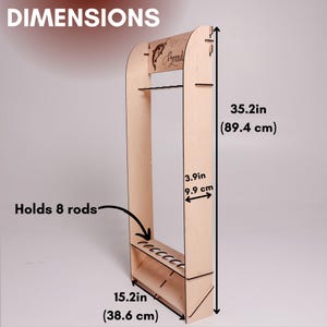 May include: A wooden fishing rod rack, 35.2 inches (89.4 cm) tall, with a shelf that holds 8 rods. The rack has a brand logo and dimensions labeled. The rack is 15.2 inches (38.6 cm) wide and 3.9 inches (9.9 cm) deep.