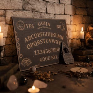 Può includere: Una tavola Ouija rettangolare in legno scuro con l'alfabeto, i numeri da zero a nove, le parole YES, NO e GOOD BYE e un grafico con sole e luna. Una planchette in legno scuro abbinata è posizionata in verticale con la scritta incisa.