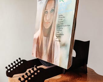 May include: A black vinyl record display stand shaped like a guitar headstock, holding a Summer Rain record by Ronald Binge. The album cover features a portrait of a person with long hair and a tracklist including Love Story and Lara's Theme.