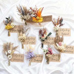 May include: A collection of dried flower bouquets in various colors, including yellow, orange, purple, and white, tied with twine. Each bouquet is paired with a small card that reads "Will you be my..." followed by a wedding party role.