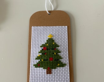 May include: A brown paper gift tag with a white cross-stitch design of a green Christmas tree with red and yellow ornaments.