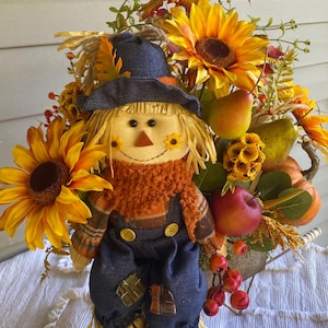 Handmade artificial floral arrangement with fruits and a scarecrow in a wheelbarrow for a beautiful fall centerpiece