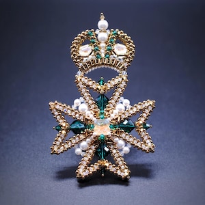 Könnte beinhalten: Eine goldene und grüne Perlenbrosche mit einer Krone und einem Sternburst-Design. Die Brosche ist mit weißen Perlen und grünen Kristallen verziert.
