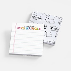 May include: A square notepad with white paper featuring blue horizontal lines and a pink vertical margin line. The top of the page displays the text 'a note from MRS. KRINGLE' in colorful letters. A second notepad with a Post-it brand logo pattern.