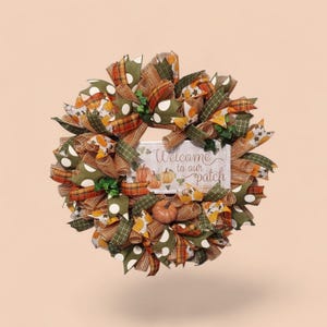 May include: A decorative wreath featuring mesh and fabric ribbons in shades of orange, green, and brown with white polka dots. A central rectangular sign displays the text Welcome to our patch with illustrations of small orange pumpkins.