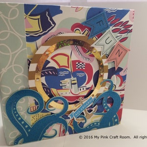 Puede incluir: Un álbum de recortes azul y dorado con temática náutica. La portada presenta una rueda de barco, un ancla y un pulpo. El texto "ALL ABOARD!" y "FUN" son visibles en la portada.