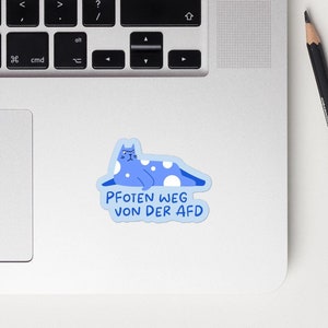 Könnte beinhalten: Eine blaue Katze mit weißen Flecken liegt auf einem weißen Hintergrund. Die Katze trägt ein blaues Halsband und hat einen weißen Pfotenabdruck auf der Brust. Der Text "PFOTEN WEG VON DER AFD" steht unter der Katze.