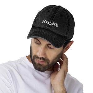 May include: A black vintage washed denim baseball cap with white embroidered text that reads "FCK U AFD" and a smiley face.
