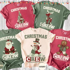 May include: A collection of Christmas-themed t-shirts in various colors, including red, green, and ivory. Each shirt features a festive graphic: a Christmas tree, reindeer, Santa Claus, snowman, and gingerbread man. The word "CHRISTMAS" is printed above each design.