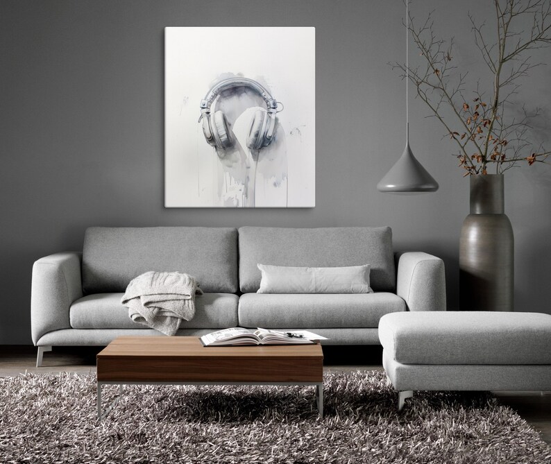 May include: A gray sofa with a throw blanket and a wooden coffee table in front of it. A gray ottoman is to the right of the sofa. A gray wall with a white canvas print of a pair of headphones hanging on it.
