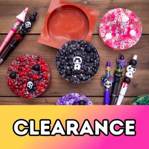 May include: A collection of craft supplies including five pens with character toppers, three circular resin coasters filled with beads and letter cubes, and one square silicone mold. The word CLEARANCE is printed in bold black letters.