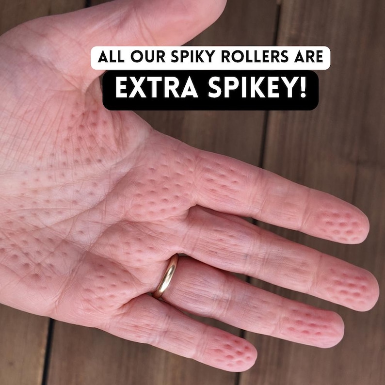 K&ouml;nnte beinhalten: Nahaufnahme einer Hand mit goldenem Ring, die eine strukturierte Oberfl&auml;che mit kleinen, gleichm&auml;&szlig;ig verteilten Erhebungen zeigt. Der Text "ALL OUR SPIKY ROLLERS ARE EXTRA SPIKEY!" ist in einem wei&szlig;en und schwarzen Banner zu sehen.