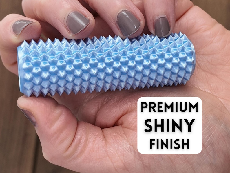 K&ouml;nnte beinhalten: Ein hellblaues, zylindrisches Massageger&auml;t mit einer strukturierten, stacheligen Oberfl&auml;che. Das Werkzeug wird in einer Hand gehalten und zeigt den Text "PREMIUM SHINY FINISH" in einem wei&szlig;en Feld.