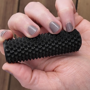 Könnte beinhalten: Ein schwarzes Massagegerät in zylindrischer Form mit einer strukturierten Oberfläche aus kleinen, erhabenen Punkten. Das Handgerät wird in der Hand einer Person gehalten, um sein Design zu zeigen. Dieses Massagegerät ist für die Muskelentspannung konzipiert.