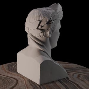 May include: A white bust of a person wearing a laurel wreath, set against a black background. The sculpture is on a round table with a brown and tan marbled surface. The bust is a classical art piece.