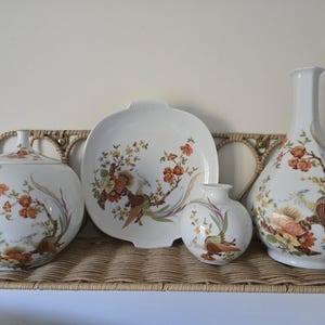 May include: A set of four white porcelain pieces featuring a floral and bird design. The set includes a lidded jar, a serving platter, a small vase, and a tall vase.