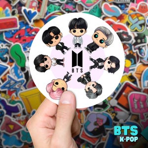May include: A round sticker with a white background and a black and white logo of the letters "BTS" in the center.  Seven cartoon characters are arranged in a circle around the logo.  The characters are all wearing different outfits and have different hairstyles.  The sticker is surrounded by a variety of colorful stickers.