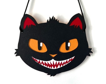 May include: Black cat Halloween decoration with red ears and orange eyes. The cat has a large, toothy grin.