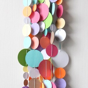 May include: A colorful paper garland with circles in various shades of pink, green, blue, orange, and brown. The circles are strung together with white thread.