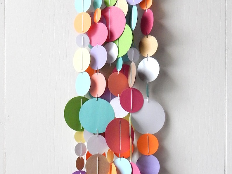 May include: A colorful paper garland with circles in various shades of pink, green, blue, orange, and brown. The circles are strung together with white thread.