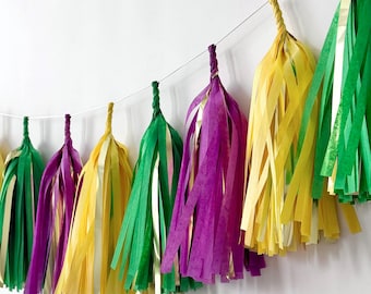 May include: A garland of tissue paper tassels in green, yellow, and purple. The tassels are strung together with a white string.
