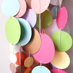 May include: A colorful paper garland with circles in various shades of green, pink, blue, yellow, and brown. The circles are strung together with white thread.