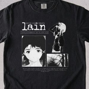 Puede incluir: Una camiseta negra de manga corta con un estampado gráfico blanco de Serial Experiments Lain. El diseño incluye el texto 'lain', un retrato en primer plano de un personaje, una figura silueteada, una pequeña escena abstracta y texto.