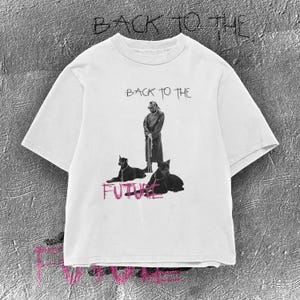 Könnte beinhalten: Ein weißes Kurzarm-T-Shirt mit einer schwarz-weißen Grafik einer Person, die mit zwei Hunden an der Leine steht. Der Text BACK TO THE ist in Schwarz über der Grafik gedruckt und das Wort FUTURE ist in Pink unter der Grafik gedruckt.